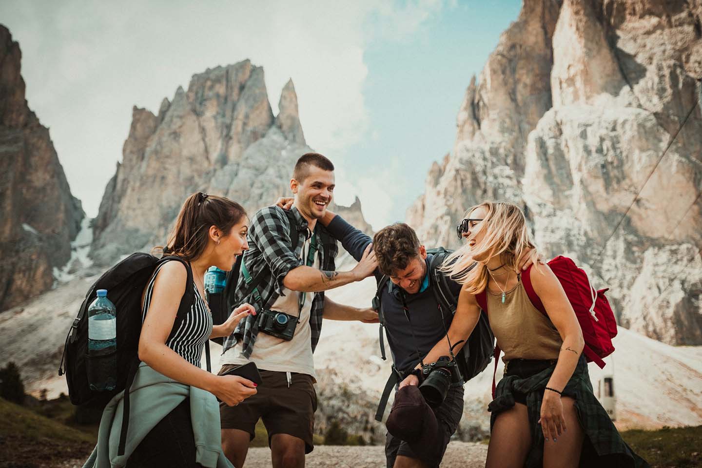 group of friends laughing, playing, and having fun with mountains behind them during travel