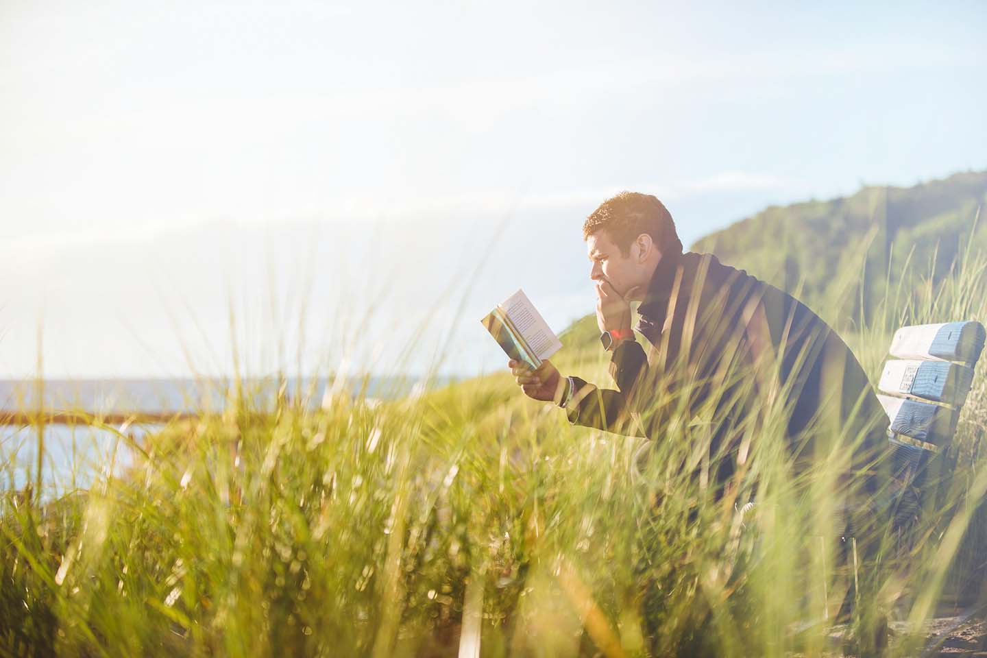 a man reading intently at the middle of grass field during daylight