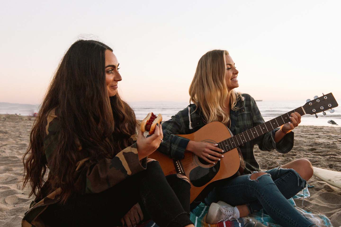 two women playing guitar on the beach