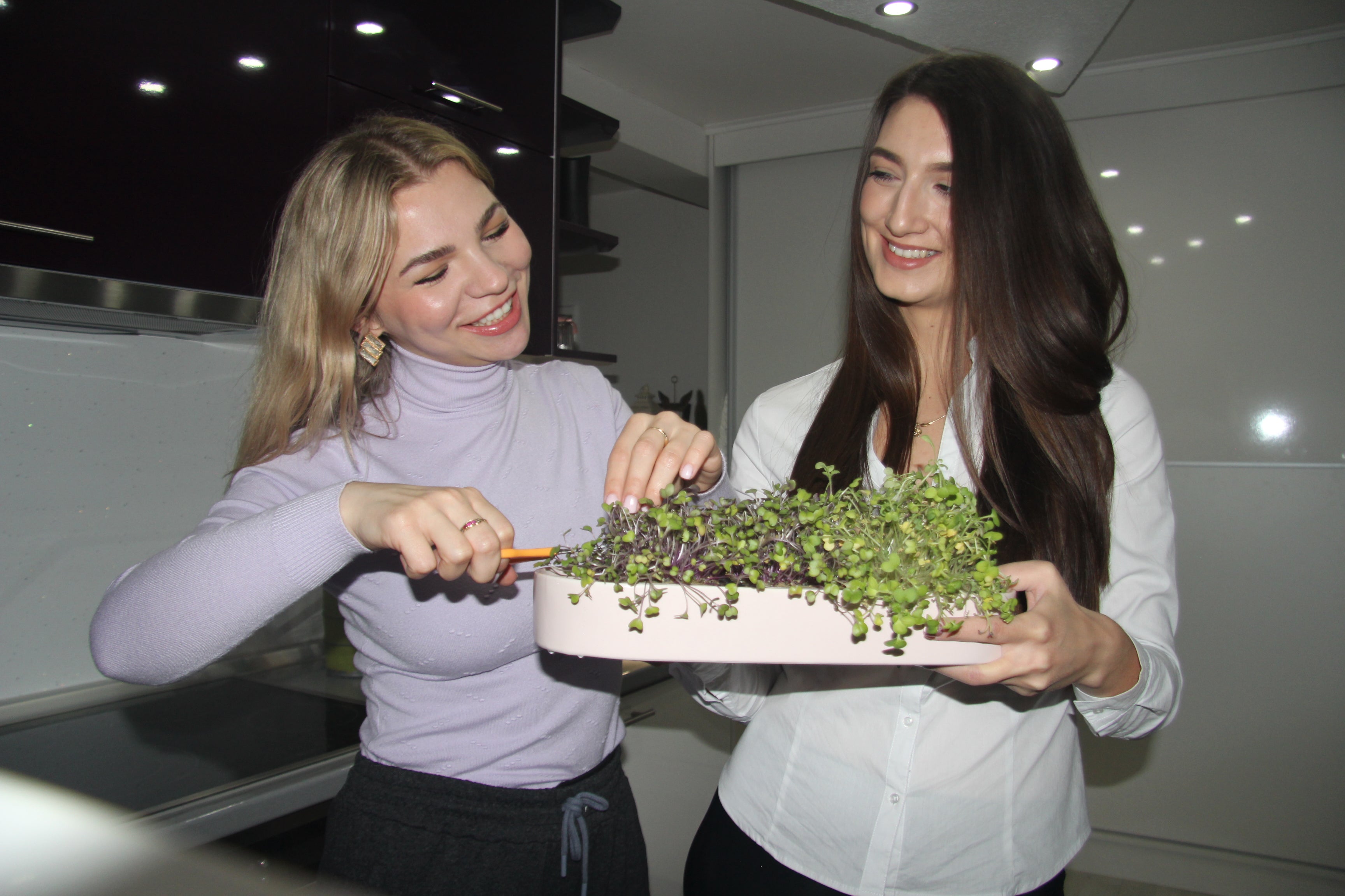 Two young women with their ingarden full of grown microgreens, ready to harvest.