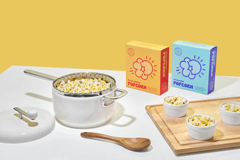 Cream Popsmith Popper filled with popcorn next to boxes of Oh Sooo Buttery and Classic Kettle Popcorn