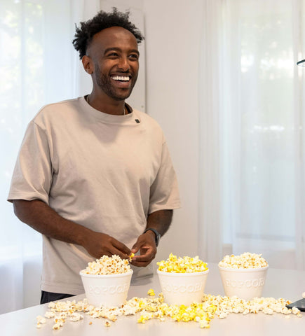 smiling man behind a counter with three different bowls of popcorn