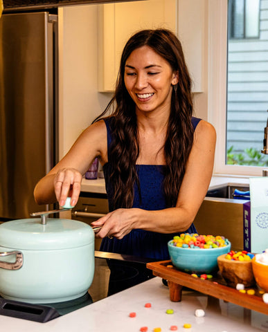 woman smiles as she turns the crank of a stovetop popcorn popper