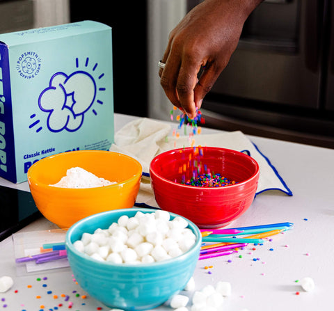 Classic Kettle Popcorn kit and bowls of powdered sugar, marshmallows, and sprinkles on a white counter