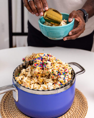 Person scoops birthday cake popcorn from a Popper into a smaller bowl