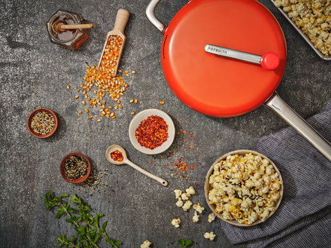 Orange popcorn popper next to a bowl of popcorn and a bunch of popcorn seasonings