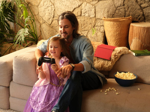 Father points while daughter holds video game controller; a bowl of popcorn sits next to them