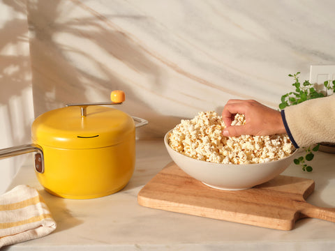 Person grabs a handful of popcorn from a white bowl