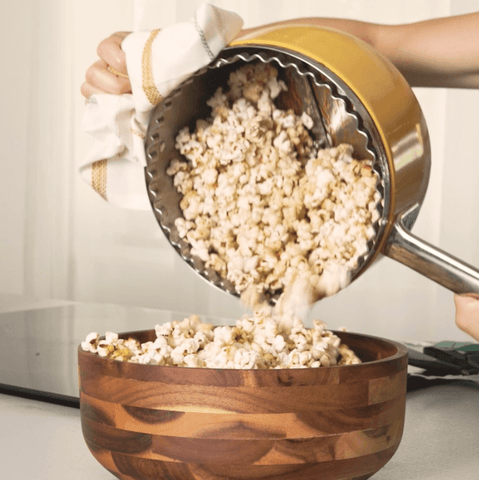 Woman pours popcorn from yellow popper into a brown bowl