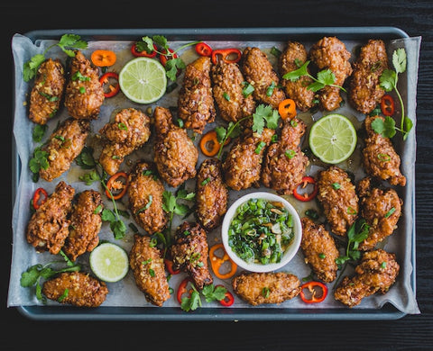 Chicken wings on a tray surrounded by lime, herbs, and peppers