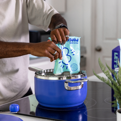 Man pours the contents of a Classic Kettle Popcorn packet onto a blue popper [42324529479873