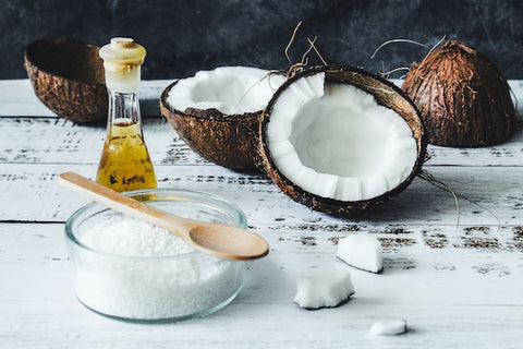 opened coconuts, a bowl of coconut flakes, and a bottle of coconut oil on a white table
