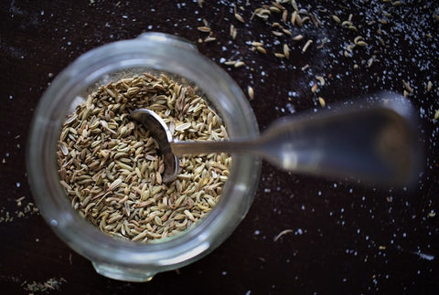 a spoon scoops some cumin seeds out of a jar