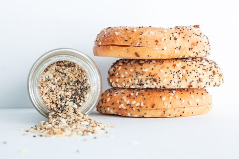 A container of everything bagel seasoning next to three bagels stacked together