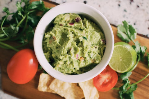 guacamole in a white bowl surrounded by lime and tomatoes