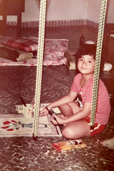 image: photo of a young girl about seven years old, smiling contentedly, holding a watercolour brush, she's painting a vase with flowers.