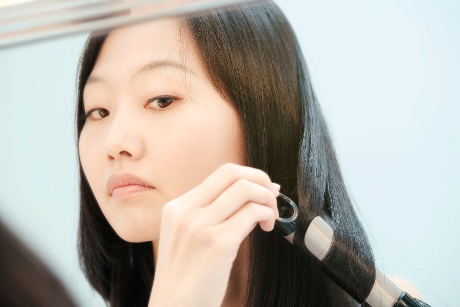 Asian person curling hair while looking in the mirror