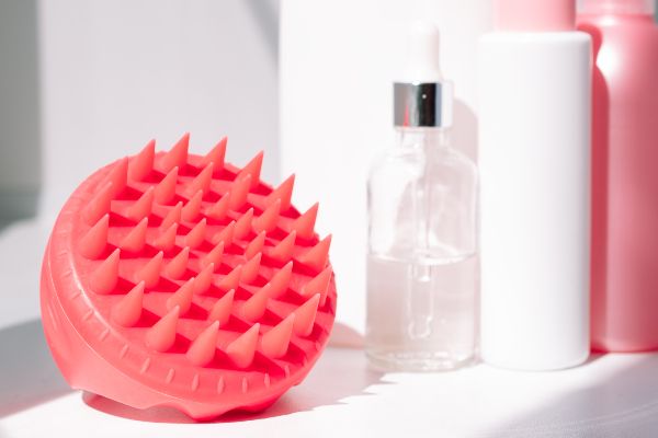 Pink scalp massager next to products on shower shelf | Mane Addicts