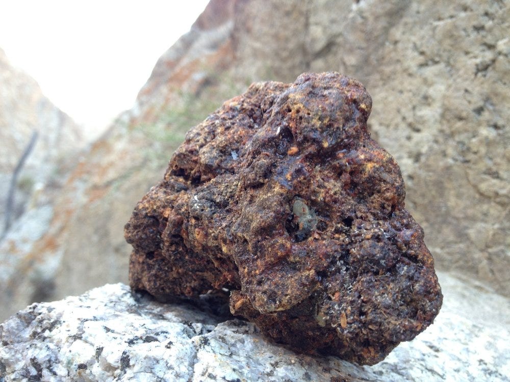 Rusty, porous rock on a granite surface with blurred background.