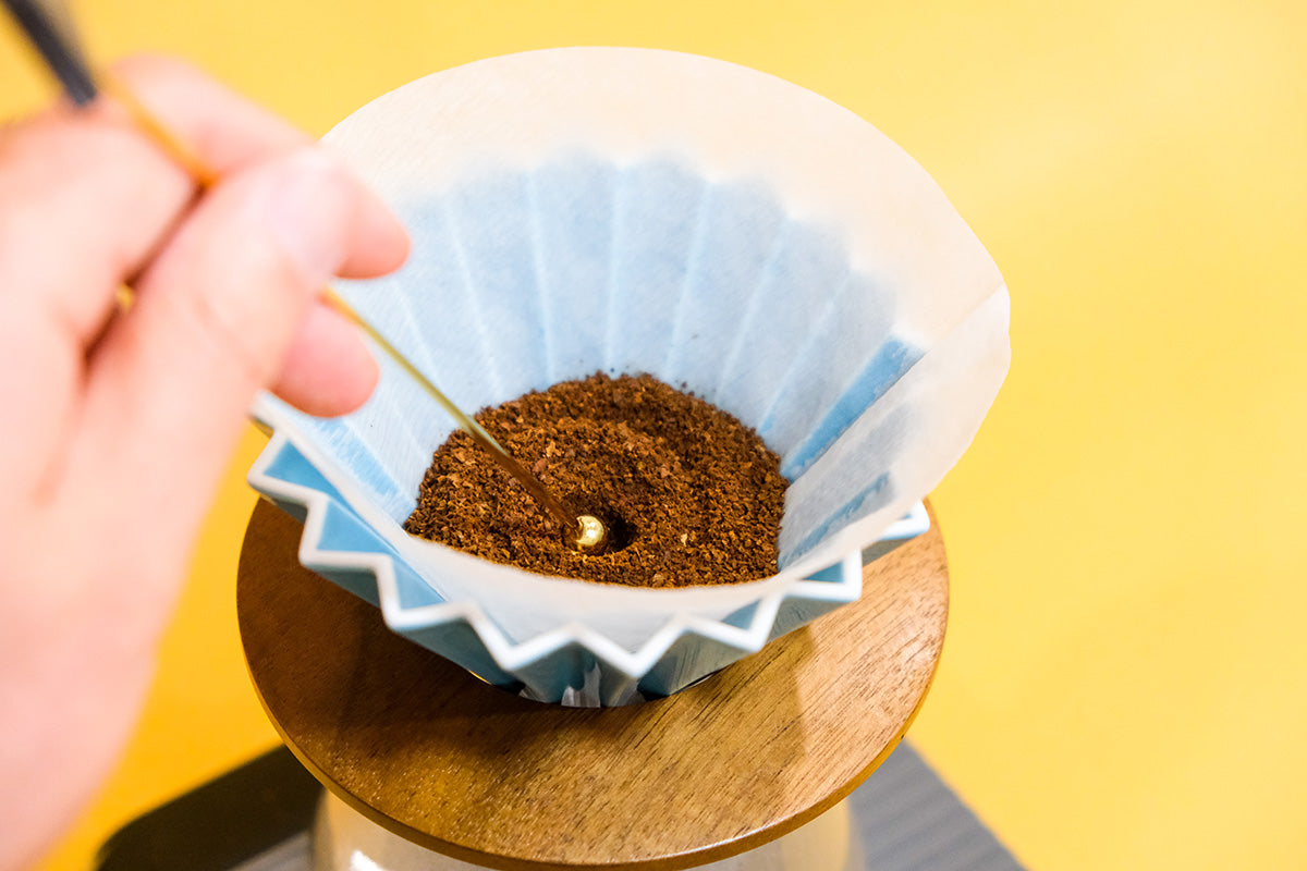 close up of a hole in the origami dripper being made in the center of the coffee grinds to optimize for pour over coffee brewing