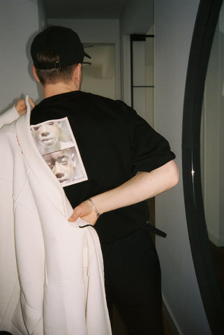 picture of the back of someone putting on a white jacket over a black t shirt