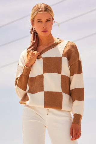 A woman poses in a mocha and checkered cream sweater. 