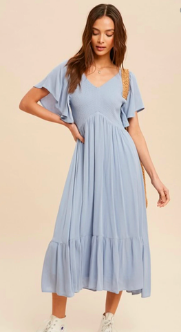A woman poses in a flowy maxi dress in a light blue shade.