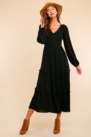 A woman in a black maxi dress, boots, and a matching hat.