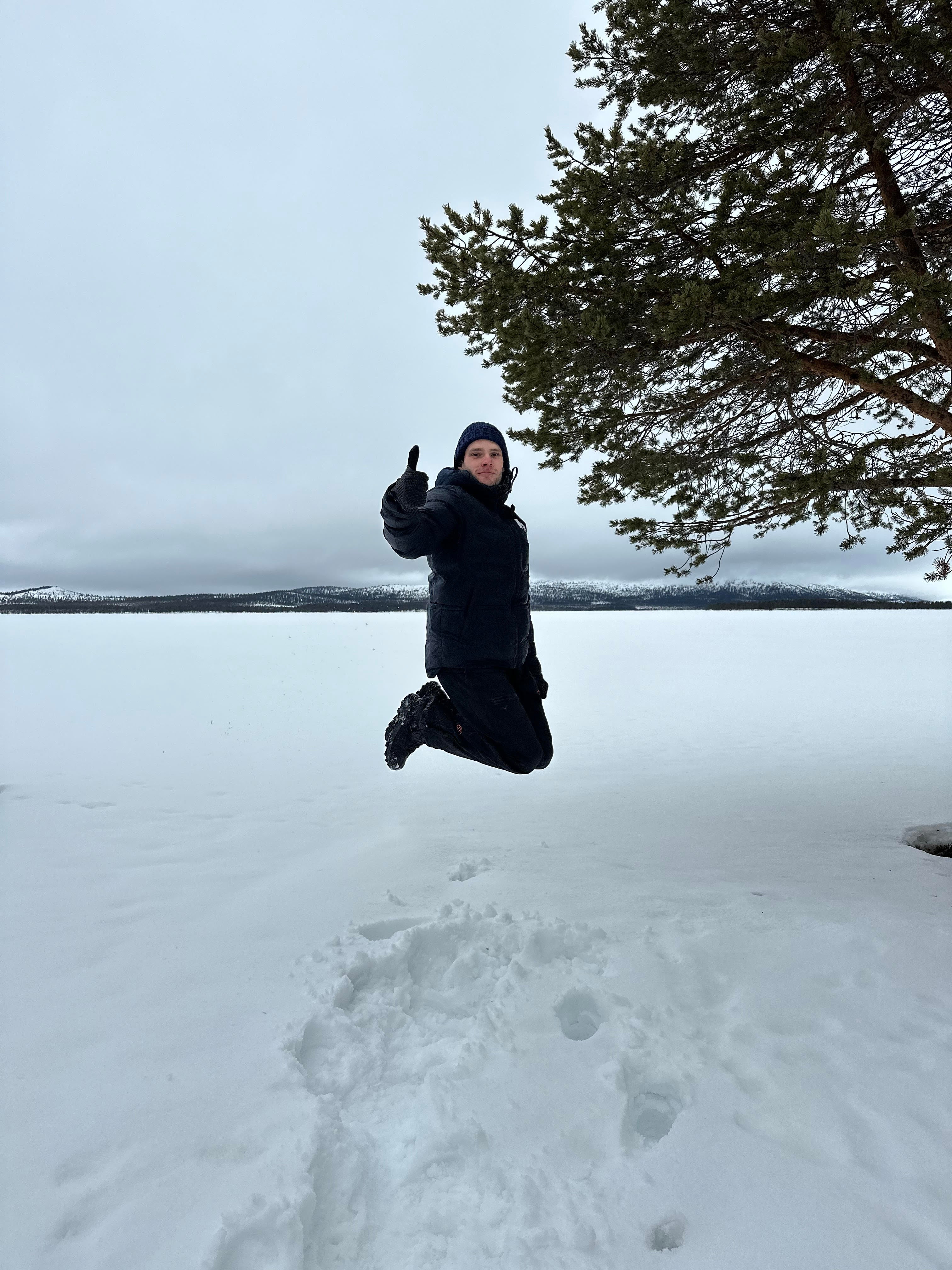 man jumping in the snow, showing a thumbs up