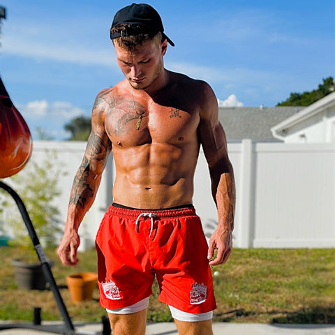 shirtless man wearing red 2 in 1 hybrid gym shorts with white compression liners standing outside looking towards the ground - King Killers Apparel