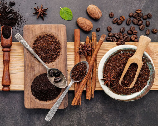 Whole coffee beasn and ground coffee beans with an array of spices on a board. Displaying the diverse flavour inherent in coffee beans