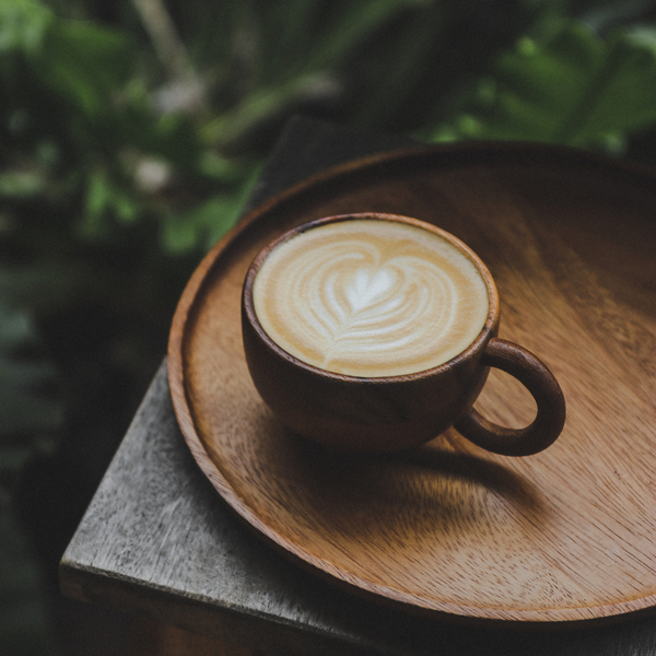 A cup of coffee on a round wooden tray, with plants in the background