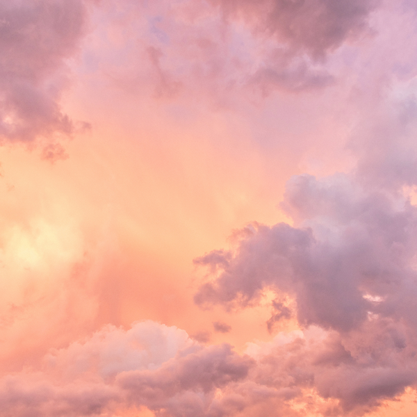 a pink and peach coloured sky with fluffy white and purple clouds