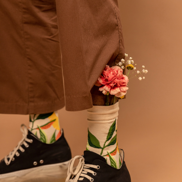 Person wearing Converse and socks, with delicate flowers (pink carnation and white gypsophilia) stuck into their sock.