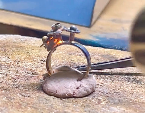 workbench area with close up of flower ring being soldered with a bench jewelers torch