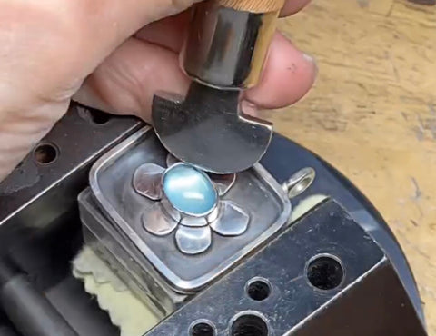 photo of bench jewelers hands setting a gemstone in a vice on an aquamarine pendant
