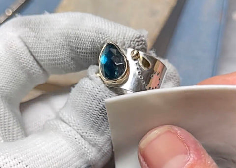 hands polishing a sterling silver and 14K solid gold ring with a blue tourmaline