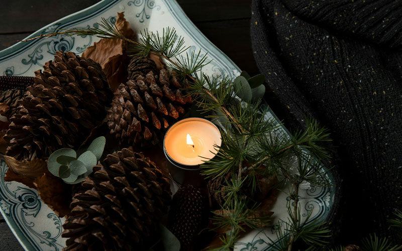 Pine cones and pine greenery surrounding a candle.