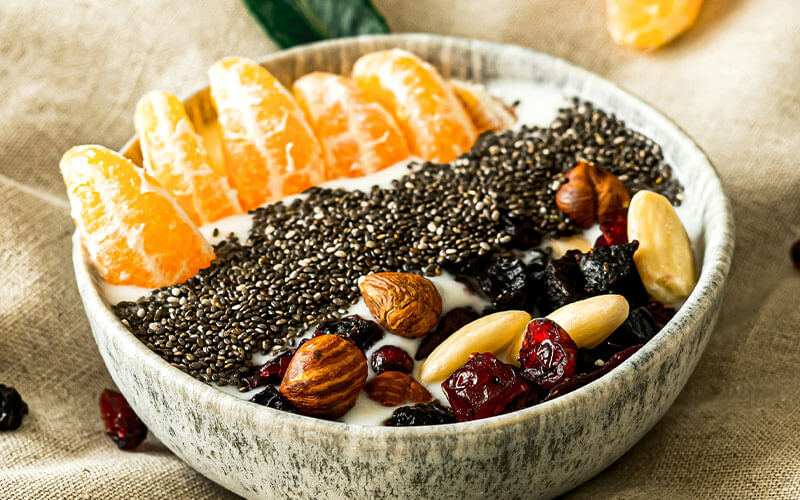 A bowl filled with yoghurt, nuts, clementine pieces and sprinkled chia seeds.