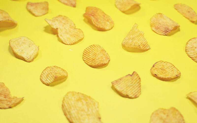 Single, ridged crisps laid out on a bright yellow board to create a repeat pattern.