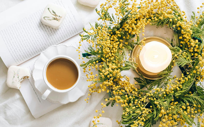 An arrangement of yellow Spring flowers with a candle and a cup of tea.