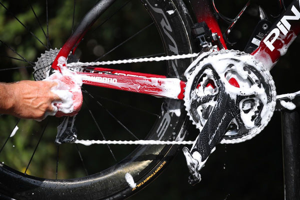 Image illustrating the first step of a DIY bike tune-up, focusing on cleaning and degreasing a bicycle, with tools and cleaning agents visibly laid out.