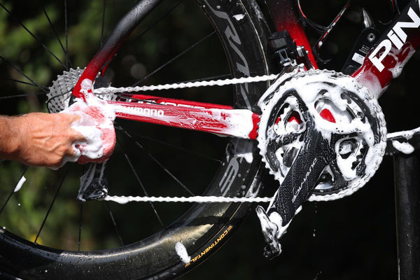 Bild, das den ersten Schritt einer DIY-Fahrradwartung zeigt, mit Schwerpunkt auf Reinigung und Entfettung eines Fahrrads, mit Werkzeugen und Reinigungsmitteln, die deutlich ausgelegt sind.