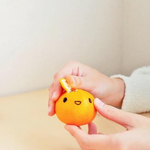 Hands peeling a mandarine orange that has a cute face drawn on it in sharpee pen.
