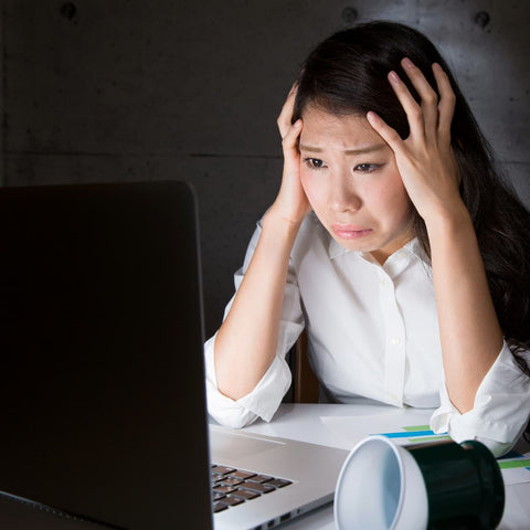 A stressed out office lady stares at her laptop screen. She has her head in her hands, and a pained look on her face. This is literally us right now.