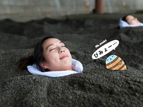 Tarutaru tries the Ibusuki Sand Bath beside a nice smiling lady. The sand is black, and he's relaxing.