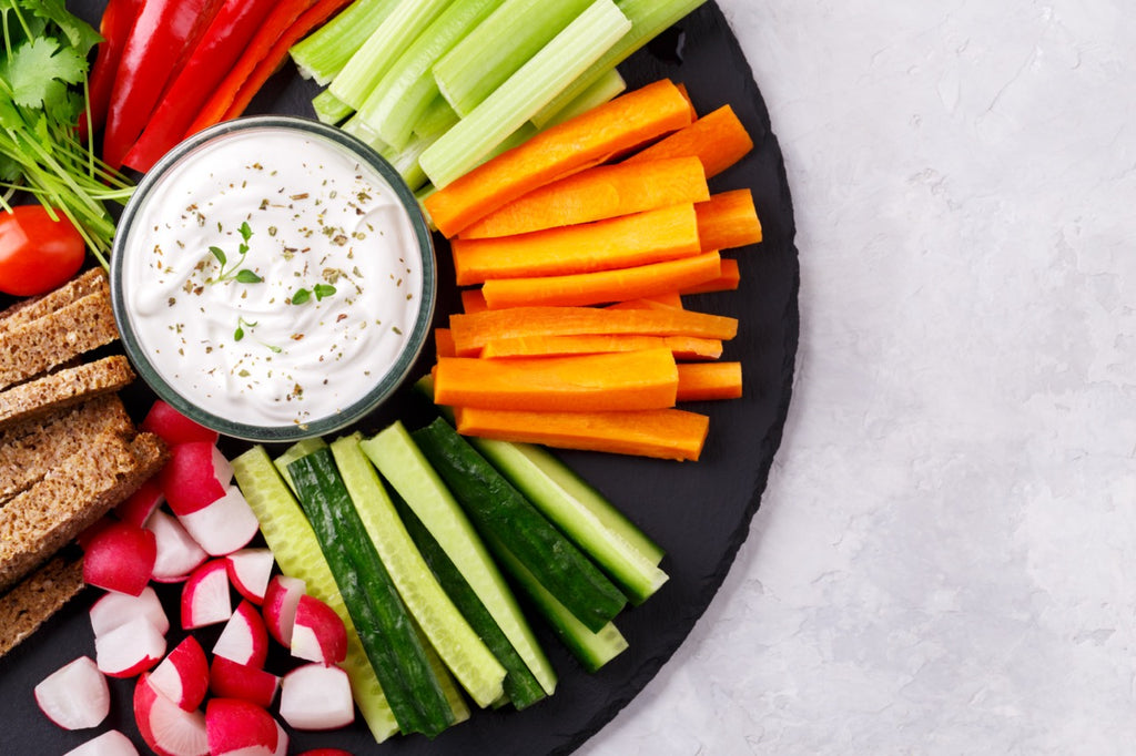 Healthy vegetables snack with yoghurt sauce on a slate stone round board, top view close up, copy space