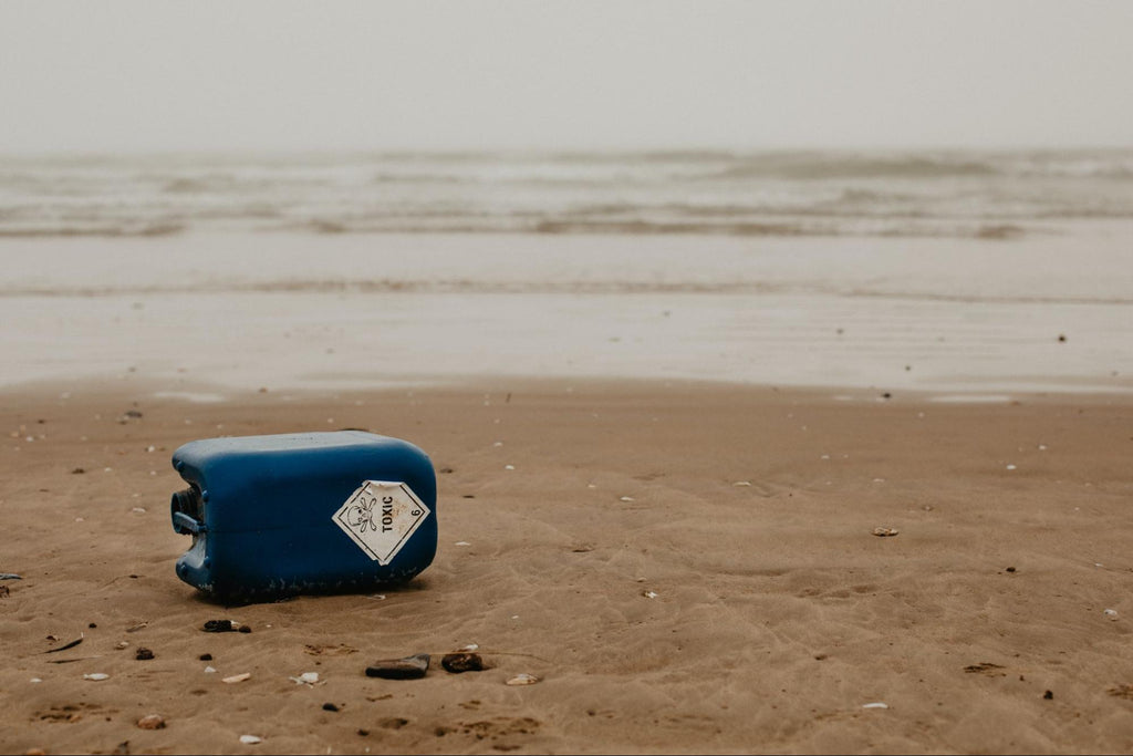 An empty container of toxic waste sits next to a body of water near a beach