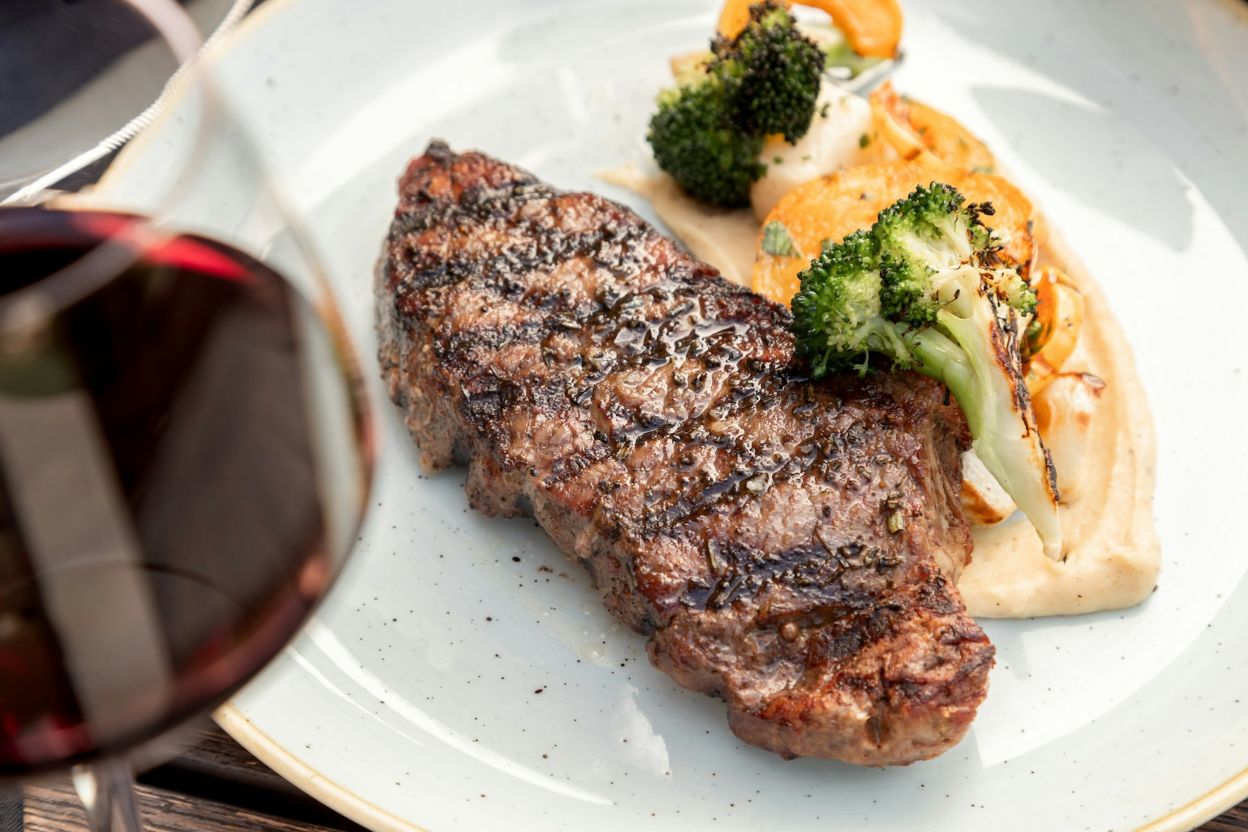 A strip of steak on a white plate with veggies