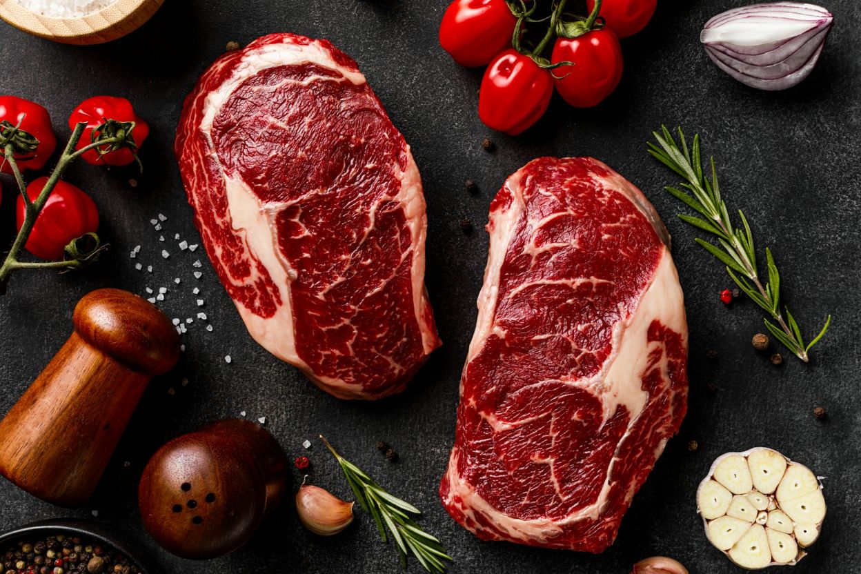 Two ribeye steaks on a table with other ingredients